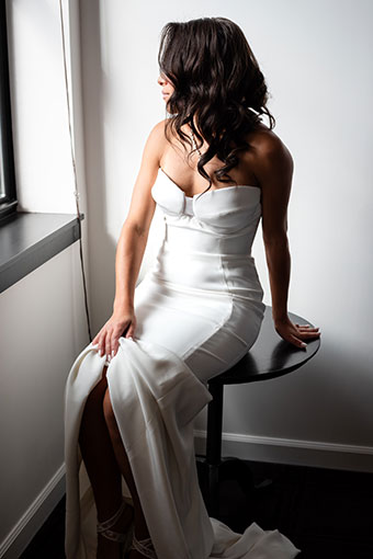 Bride, dressed, sitting on a table and looking out a window