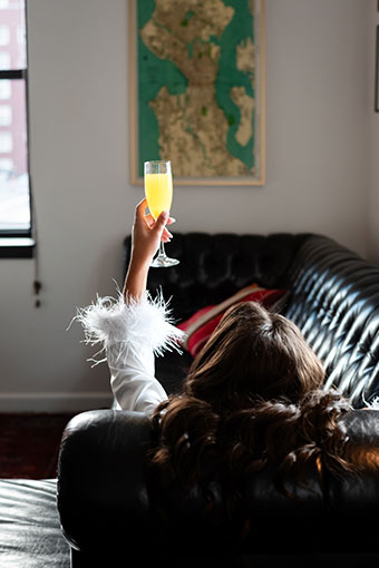 From behind: bride laying on the couch, her arm up with a cocktail in hand