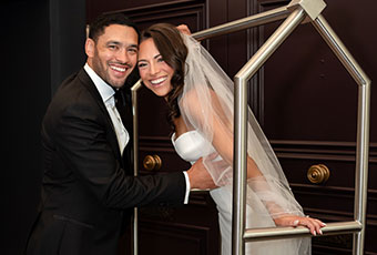 Bride and groom smile at the camera. Bride is on a bell cart