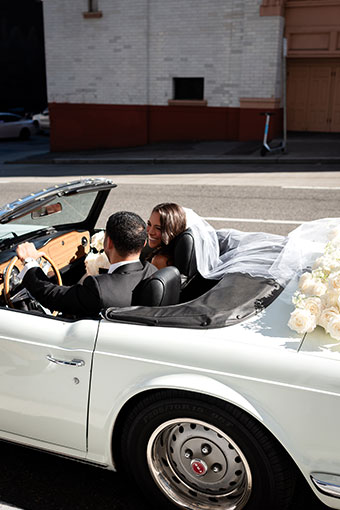 Bride and groom driving away in a white convertible, flowers on the back
